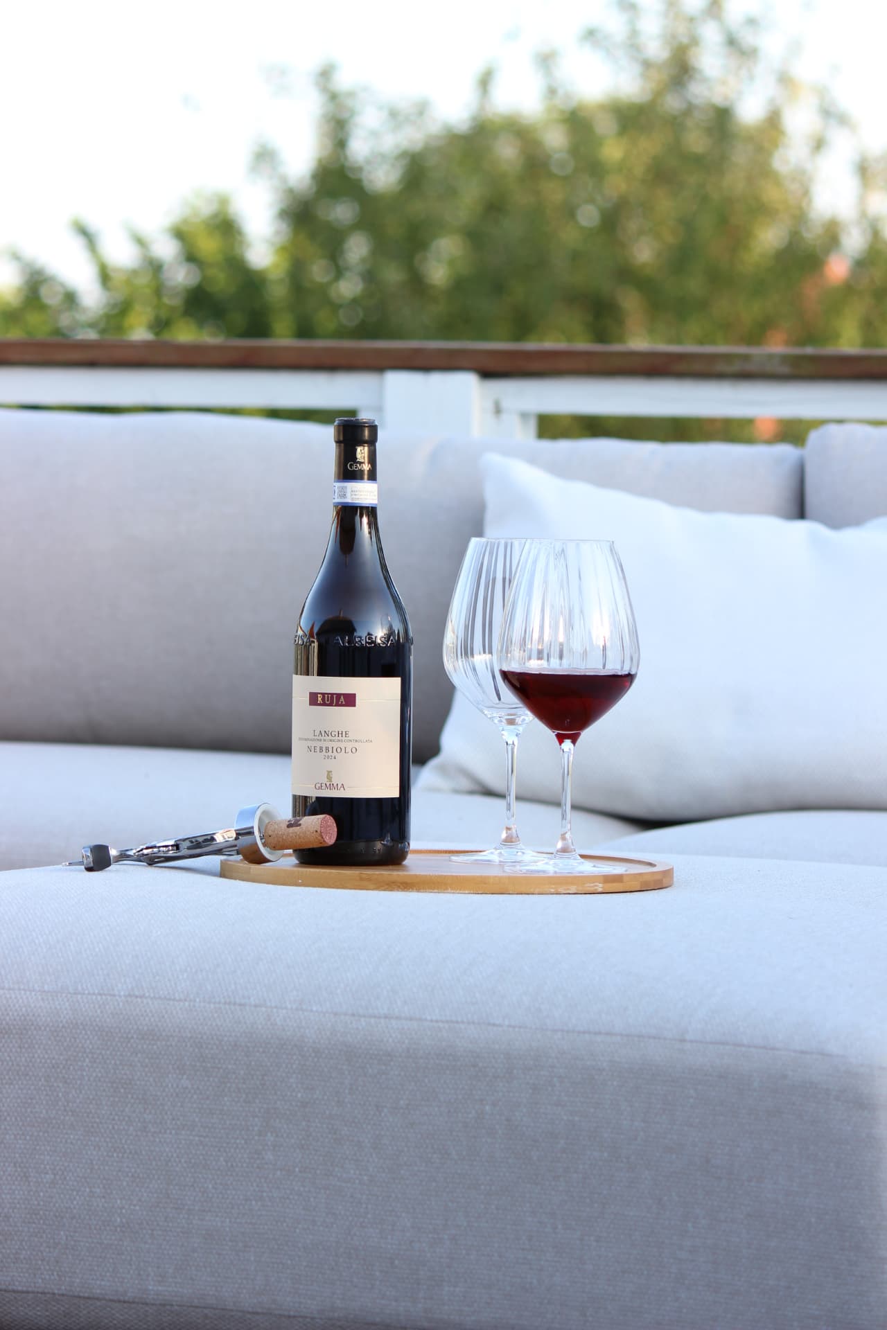 Flaske Langhe Nebbiolo, proptrækker og to vinglas på et træfad udendørs